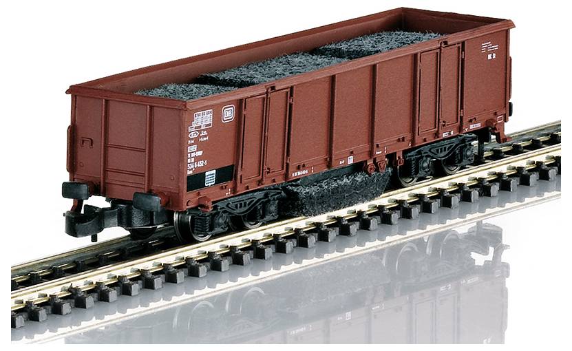 Une voiture de marchandises de train miniature remplie d'un matériau ressemblant à du charbon est posée sur une voie, présentant un design détaillé et une couleur d'extérieur rouge.