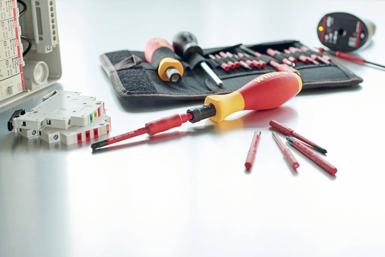 Ensemble d'outils comprenant des tournevis et des accessoires posés sur une table. À l'arrière-plan, un étui ouvert avec d'autres outils est visible.