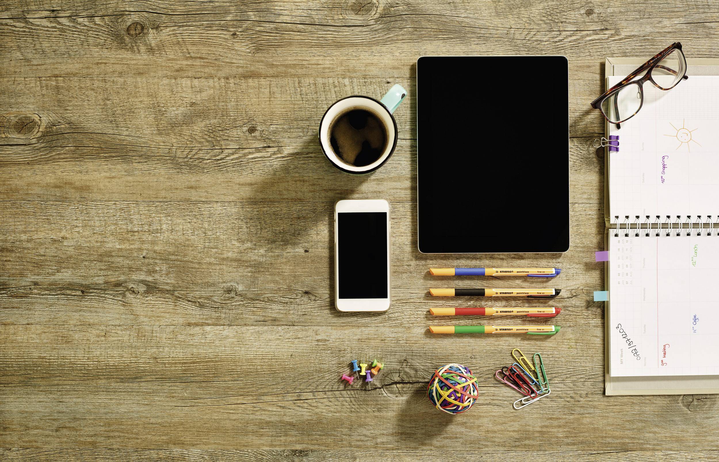 Tablette, smartphone, café, stylos, carnet sur du bois. Espace de travail avec des outils numériques et analogiques, prêt pour un travail créatif ou de la planification.