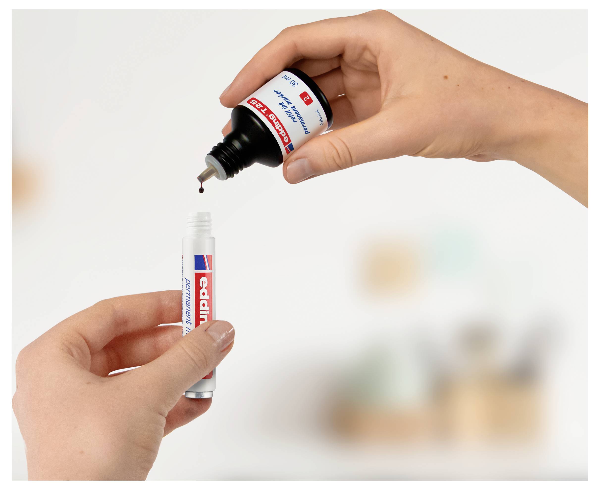 Les mains tiennent un tube et une bouteille de colle adhésive rouge, avec une goutte en train d'être distribuée dans le tube.