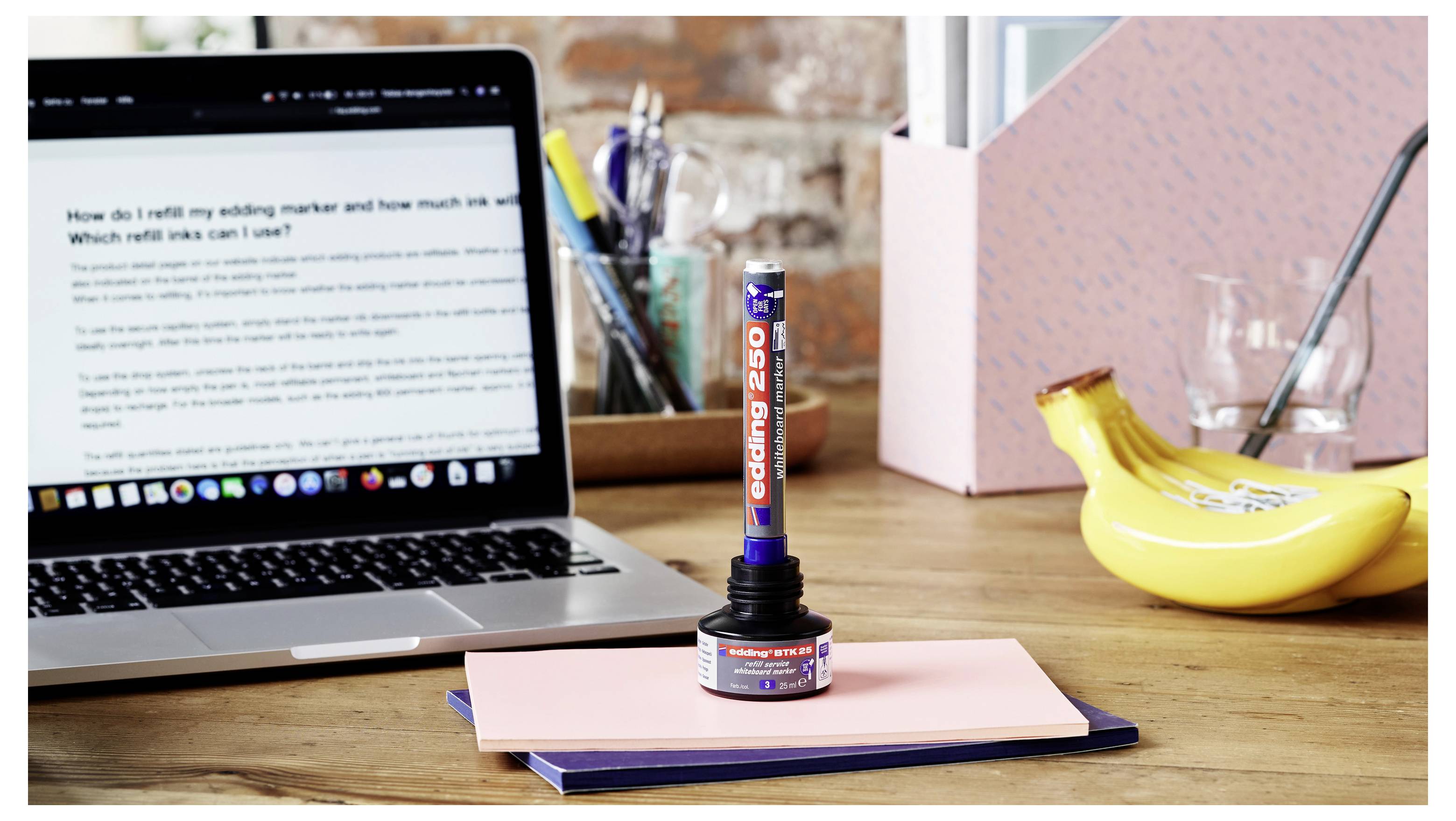 Un ordinateur portable sur un bureau à côté d'une jauge de batterie ressemblant à un bâton luminescent étiquetée « Chargement 250 » posée sur des cahiers empilés, avec une banane et un verre en arrière-plan.