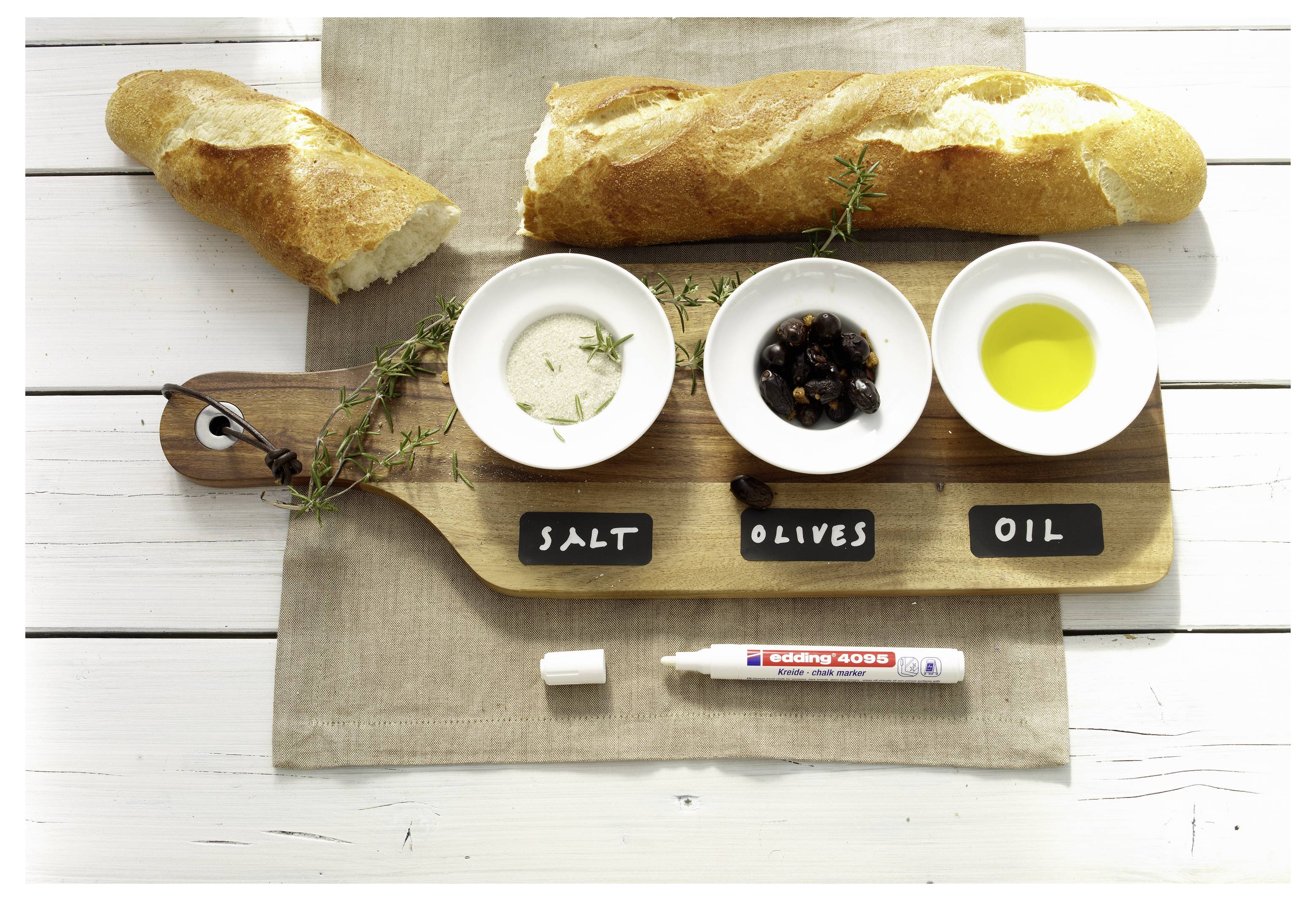 Pains avec trois bols de trempette étiquetés « SEL », « OLIVES » et « HUILE » sur une planche en bois, avec un marqueur en dessous.