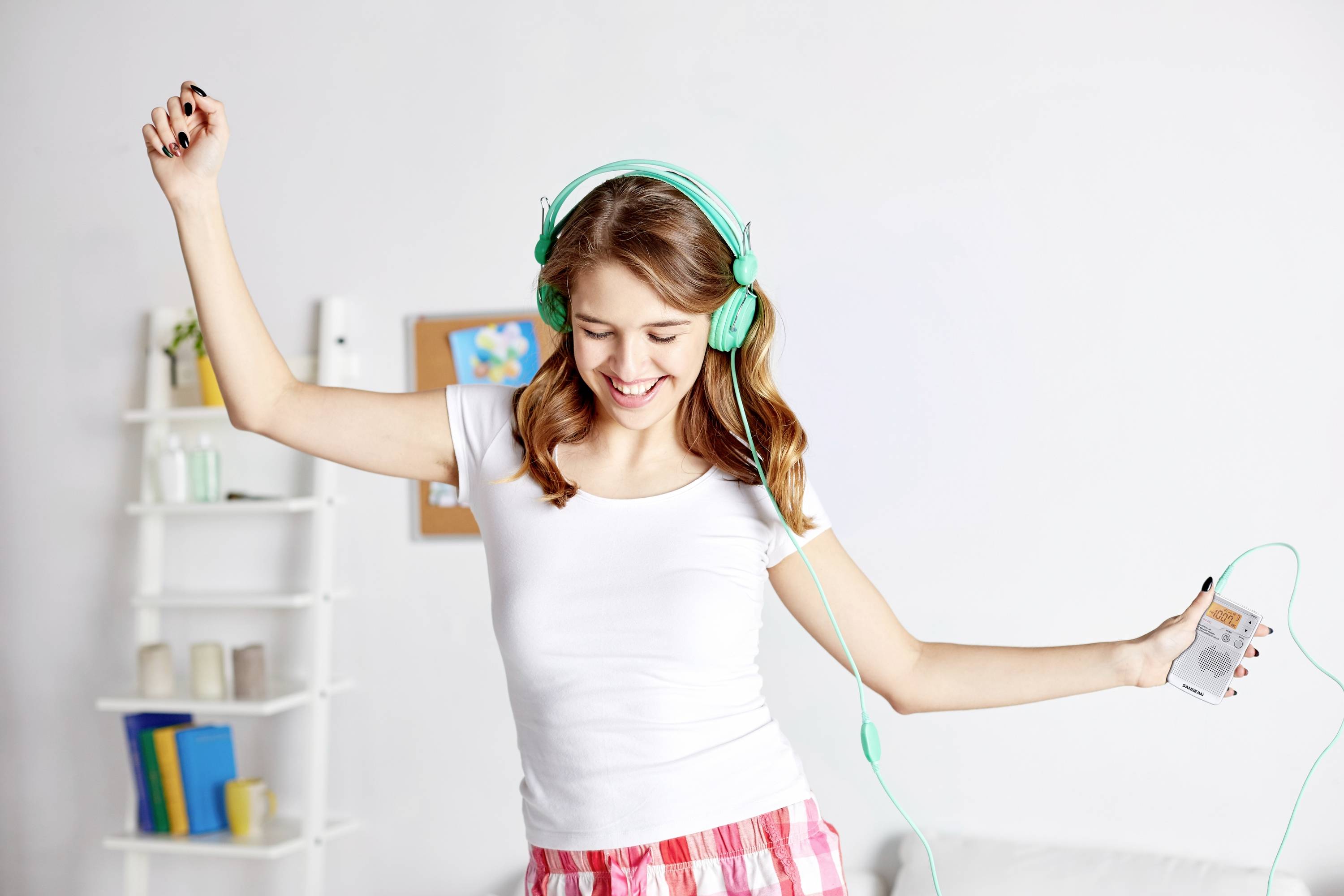 Une jeune femme danse joyeusement dans sa chambre, portant des écouteurs et tenant un lecteur de musique dans sa main.