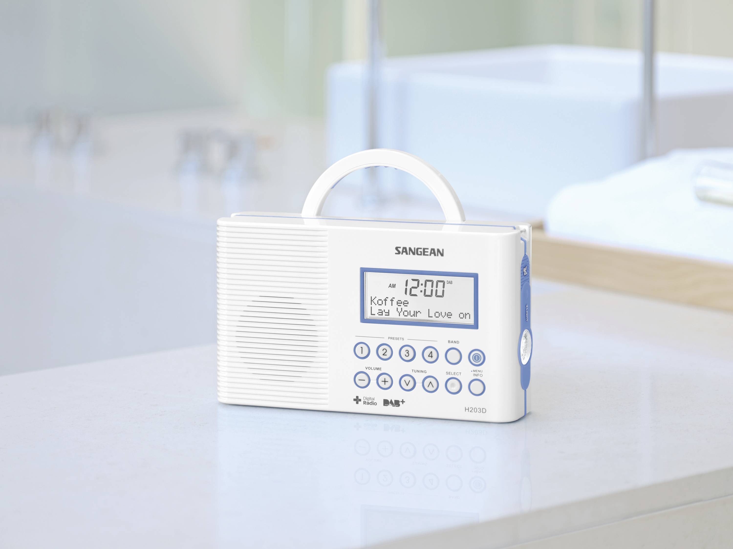 Radio portable blanc posé sur une surface de salle de bain. L'affichage indique '12:00', 'Café' et 'Lay Your Love on'.