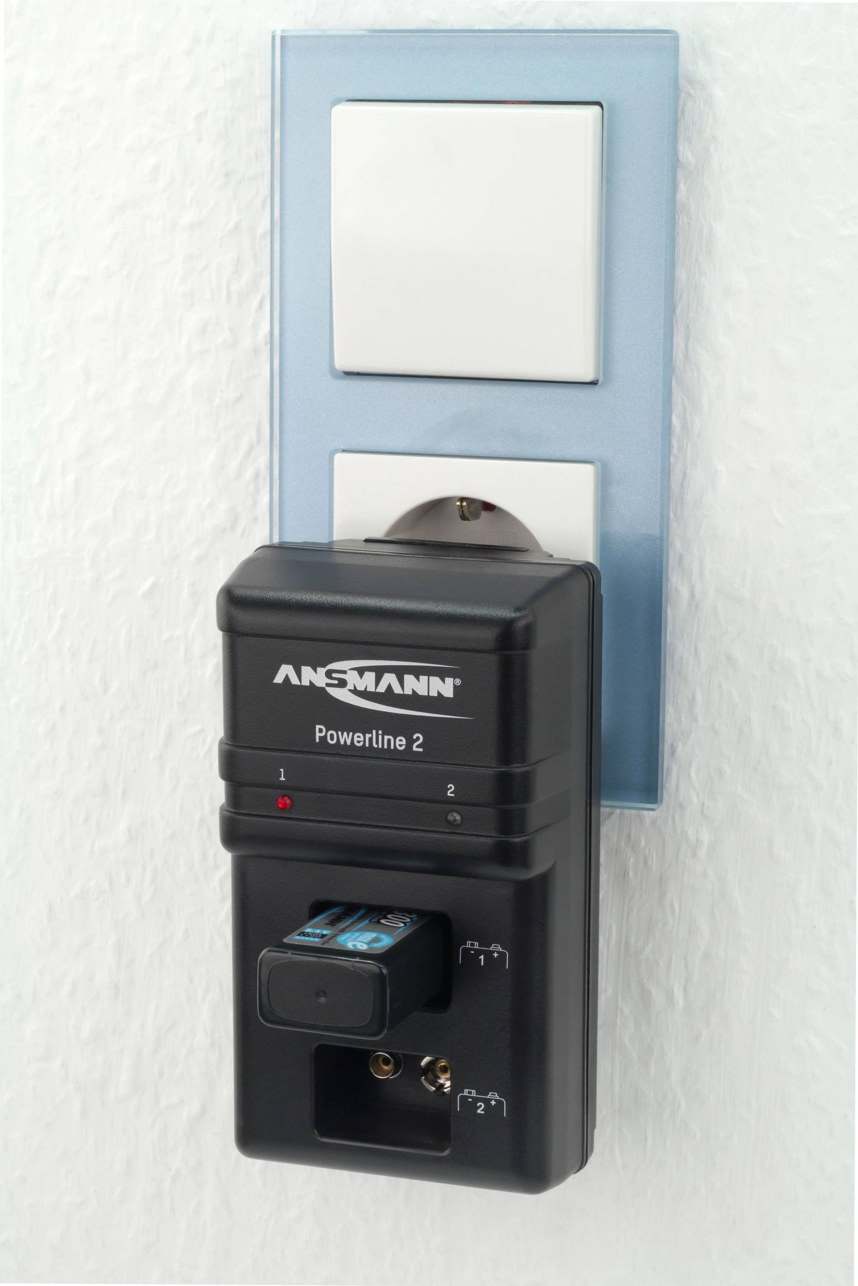 Un chargeur de la marque Ansmann est branché dans une prise murale et charge une batterie.