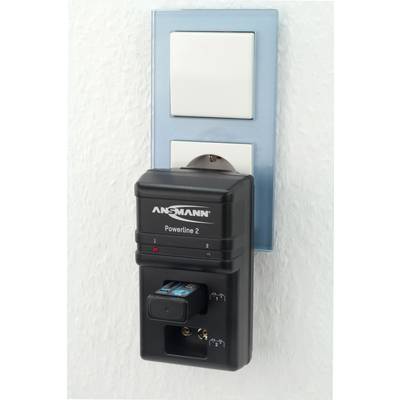 Un chargeur de la marque Ansmann est branché dans une prise murale et charge une batterie.