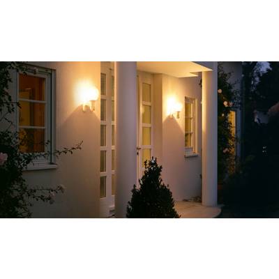 Entrée de maison éclairée le soir avec des colonnes et des plantes à côté de la porte.