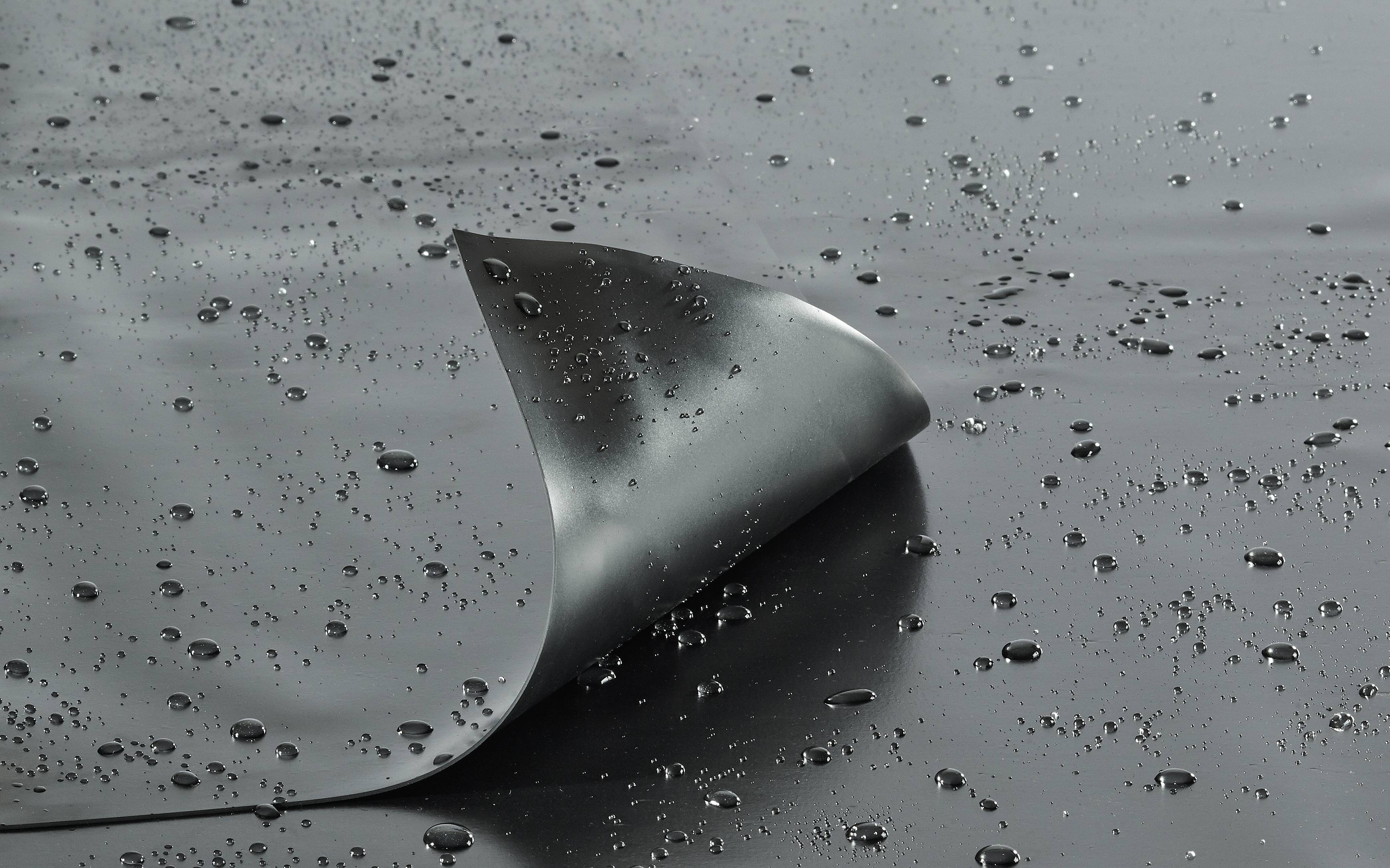 Une surface brillante, hydrofuge avec des gouttelettes d'eau et un coin légèrement soulevé pour montrer sa flexibilité et sa résistance à l'eau.