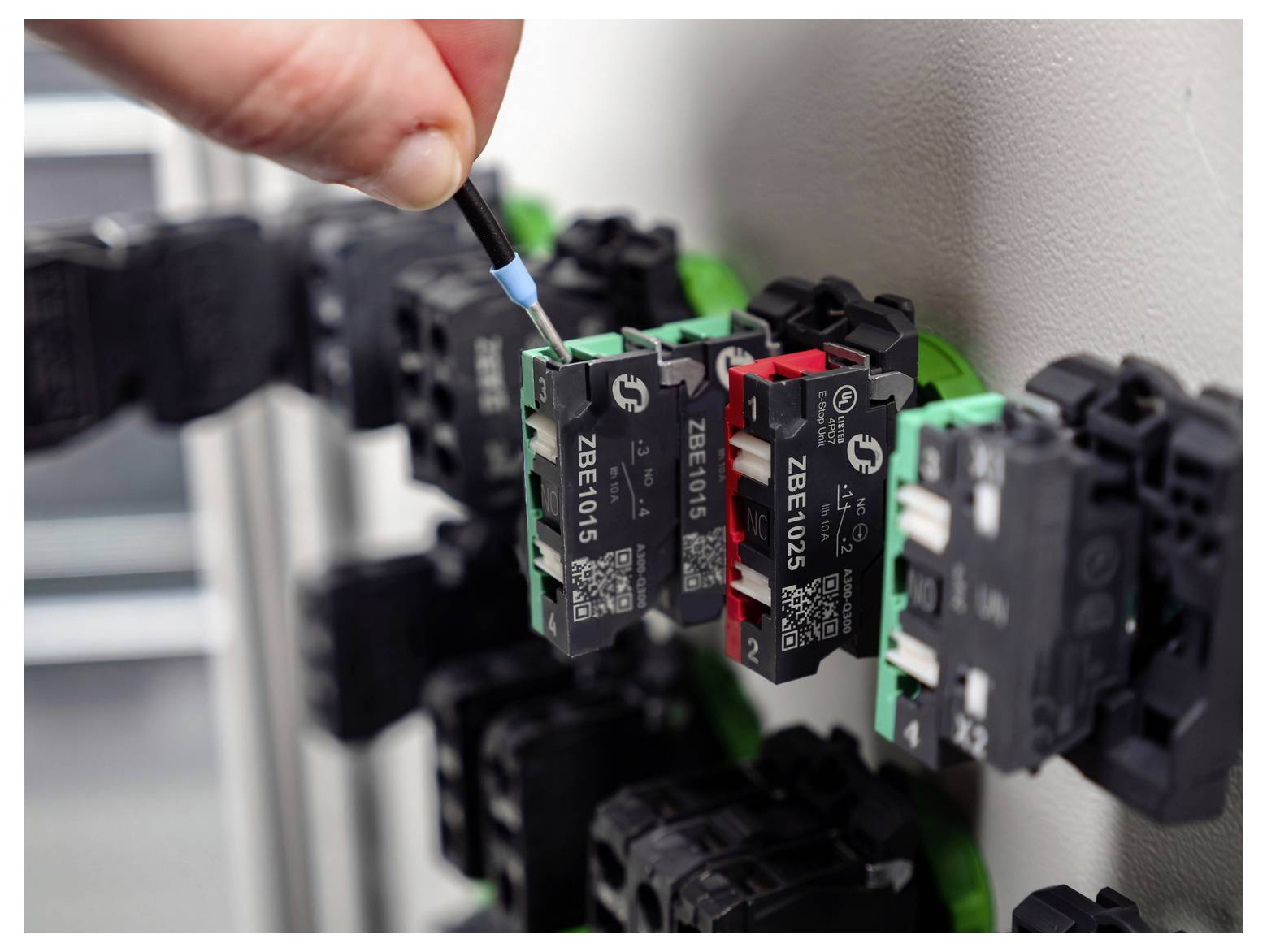 Une main utilise un tournevis pour ajuster un module de panneau de contrôle électrique avec des composants de circuit étiquetés.