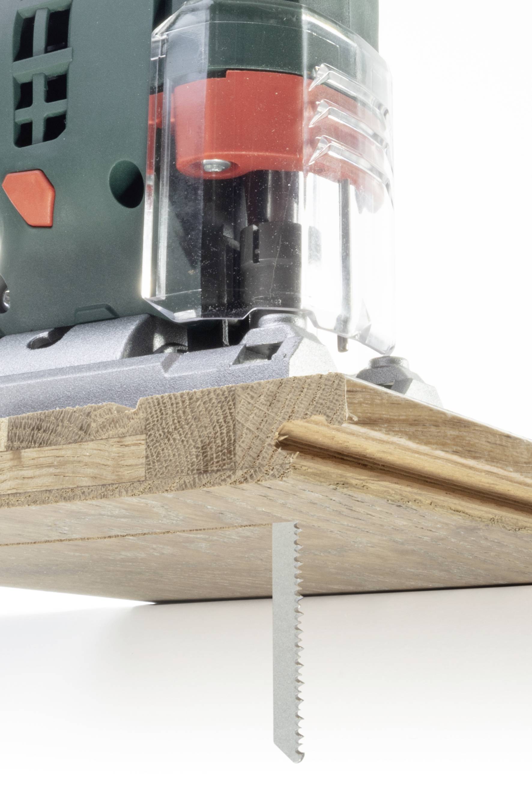 Une scie sauteuse coupe précisément à travers une planche de bois. La scie a une lame visible et une protection en plastique transparent.