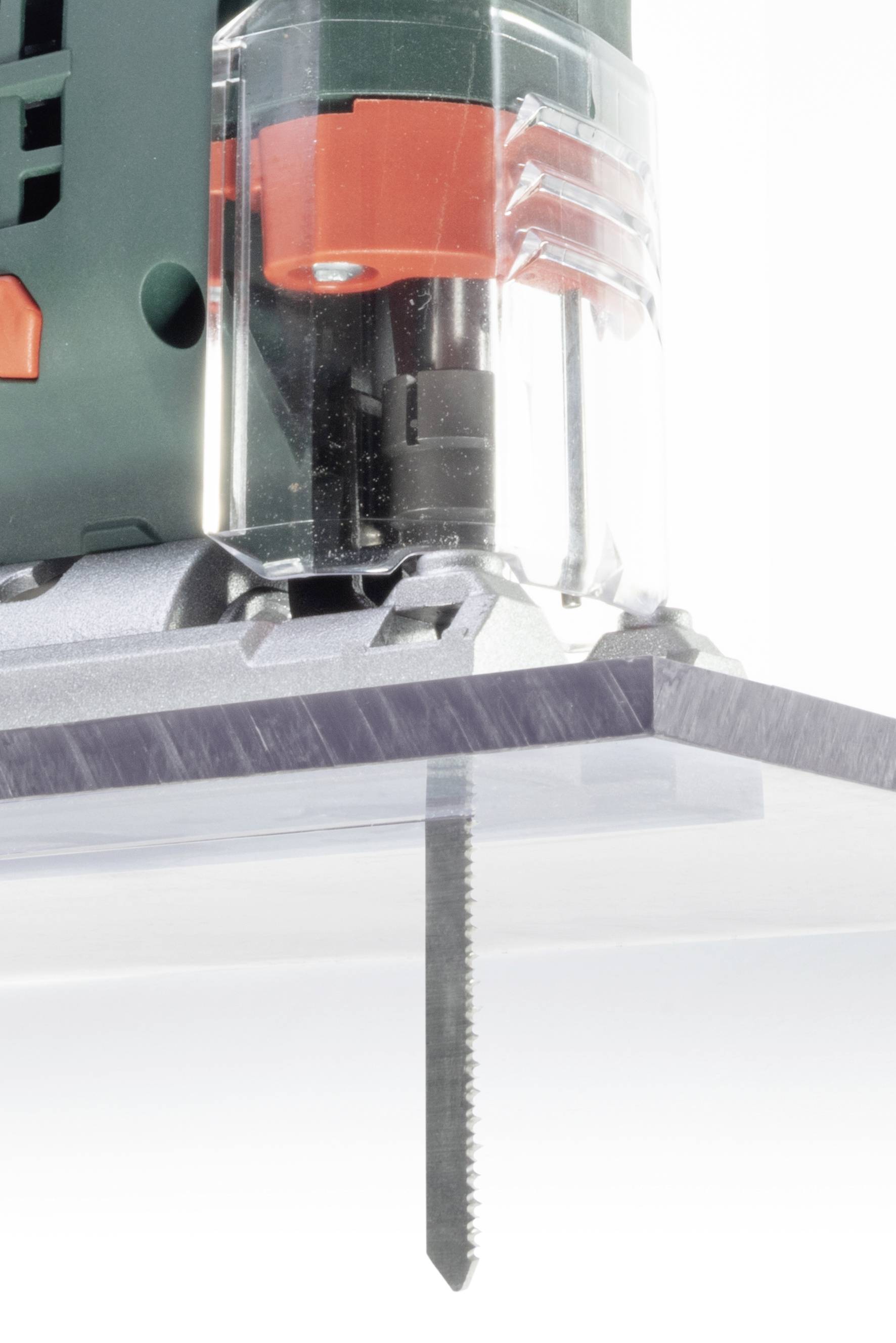 Une lame de scie sauteuse électrique coupe à travers une plaque transparente. La machine a un boîtier vert avec des éléments rouges.