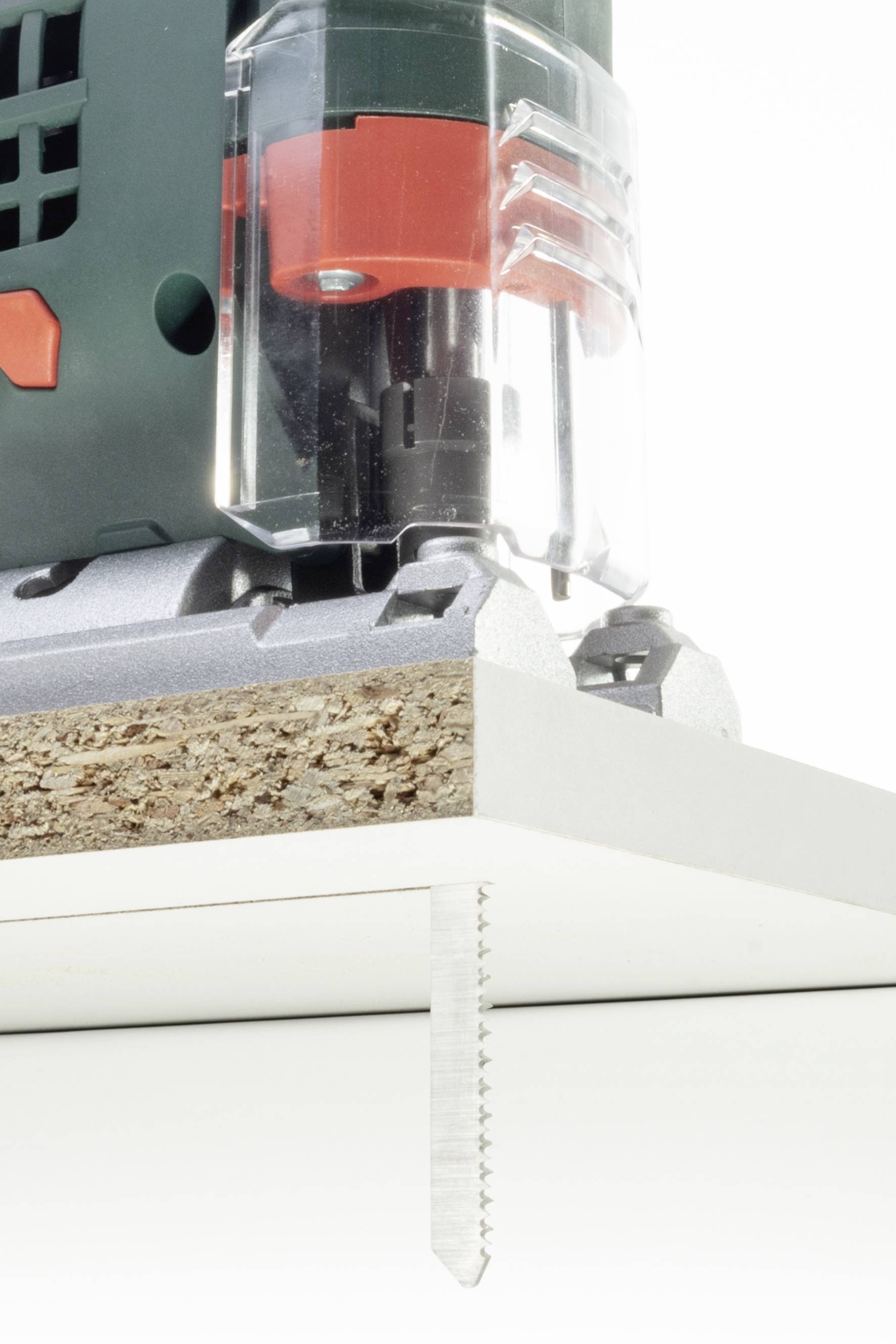 Une scie sauteuse électrique coupe une plaque de particules. La lame est visible en action, tandis que la machine perfore le matériau.