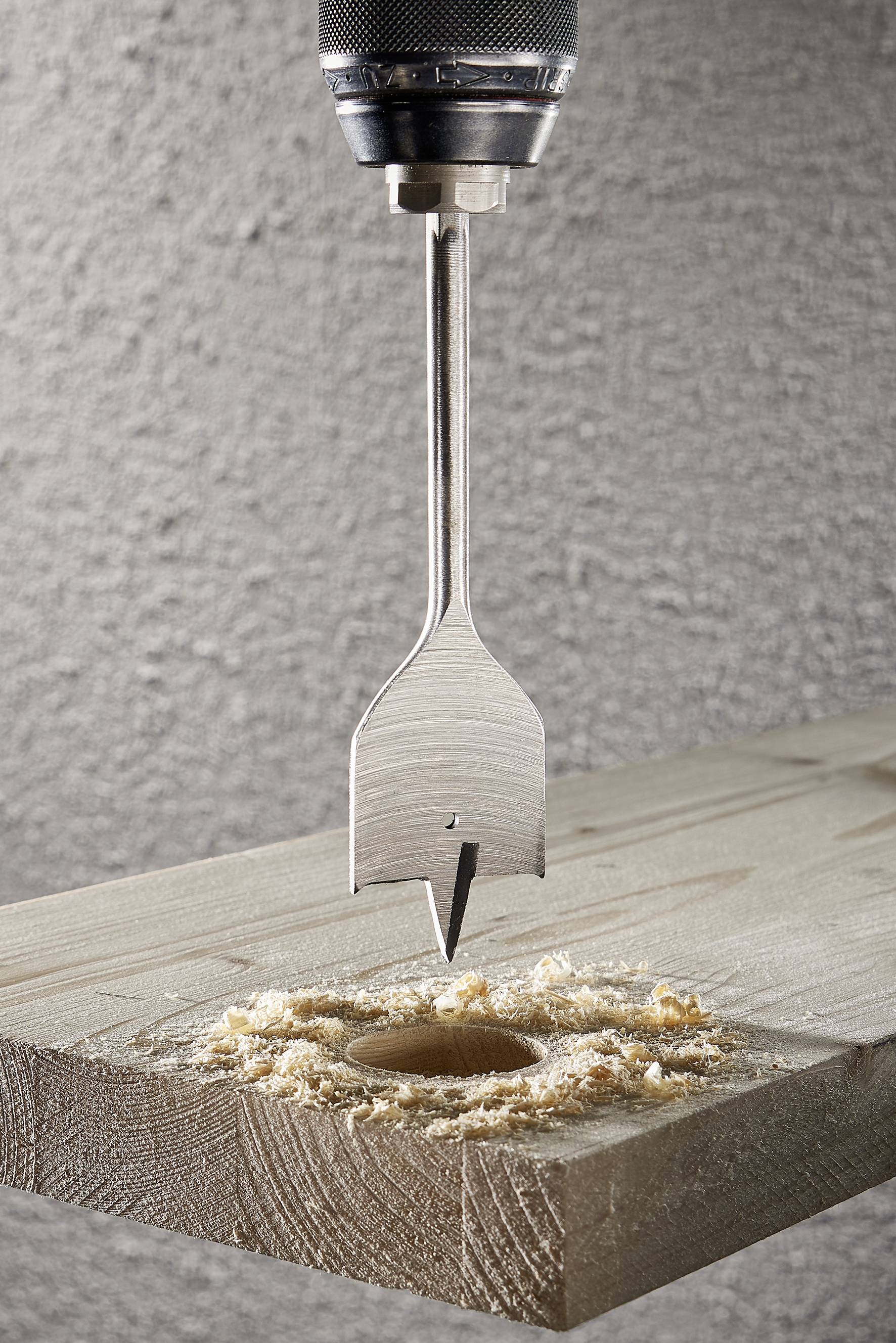 Un foret fait un trou rond dans une planche de bois, entouré de copeaux de bois.