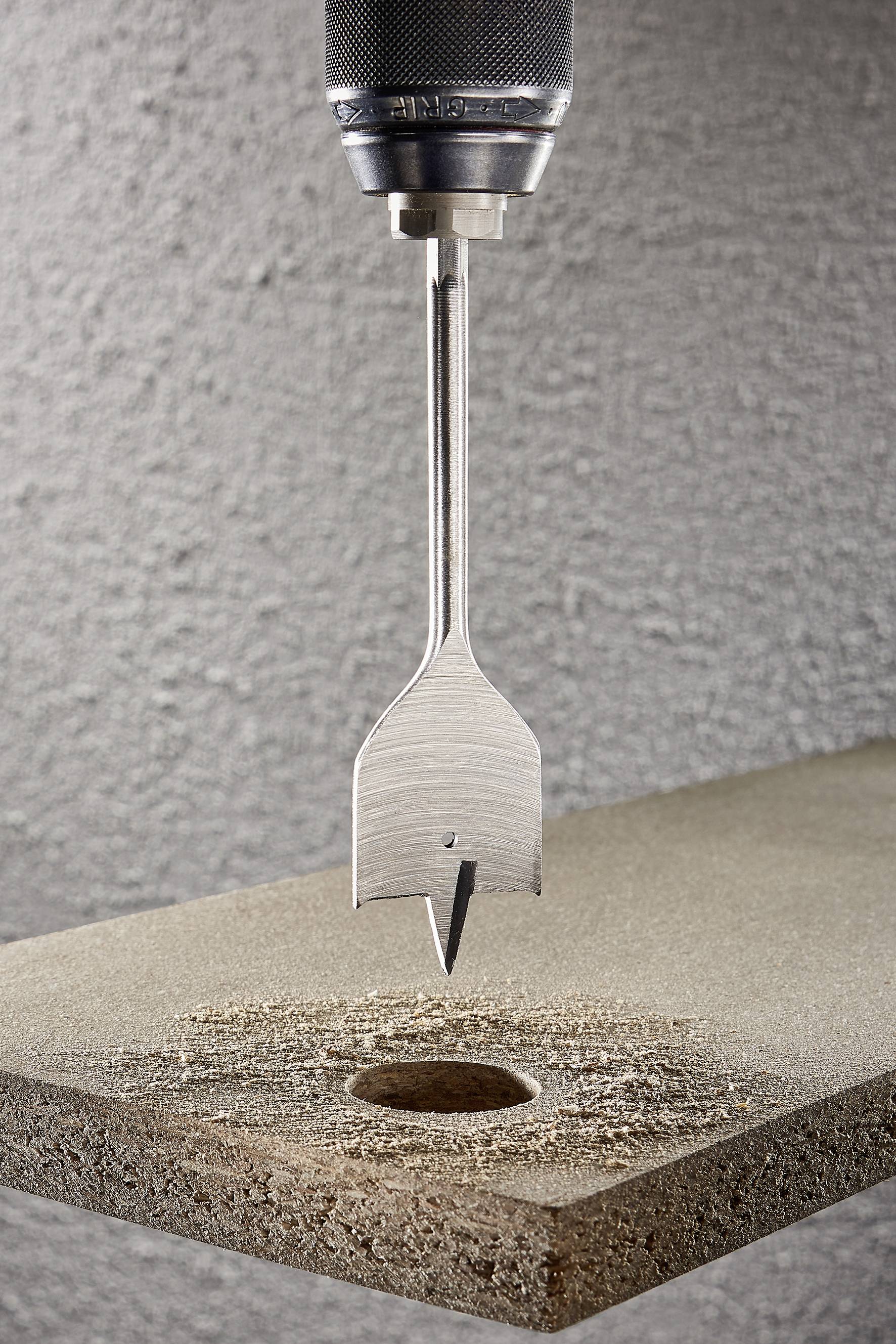 Un foret à tête plate fore un trou rond dans une planche de bois. Gros plan, mise au point sur la pointe de l'outil et le trou percé.