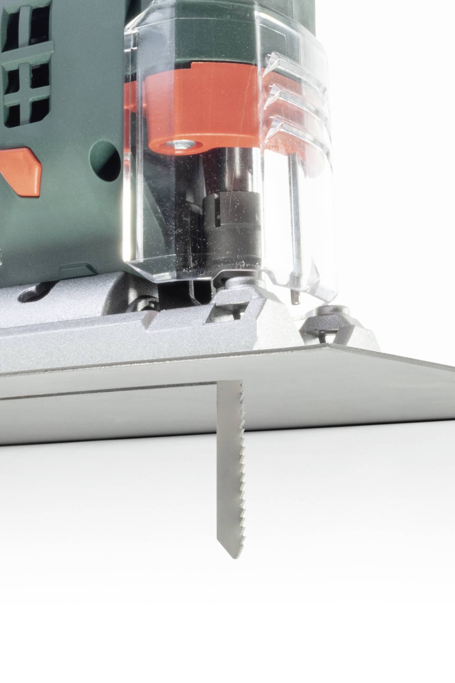 Gros plan sur une scie sauteuse prête à être utilisée. Le carter de protection de la lame est partiellement transparent, la zone de coupe clairement visible.