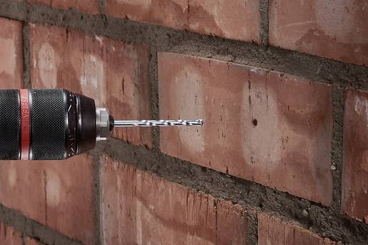 Une perceuse fore un trou dans un mur de briques. Le foret est dirigé vers le côté droit des briques.