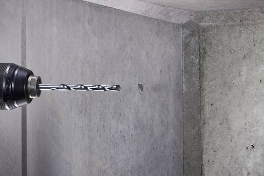 Un perceuse fore un petit trou dans un mur en béton.