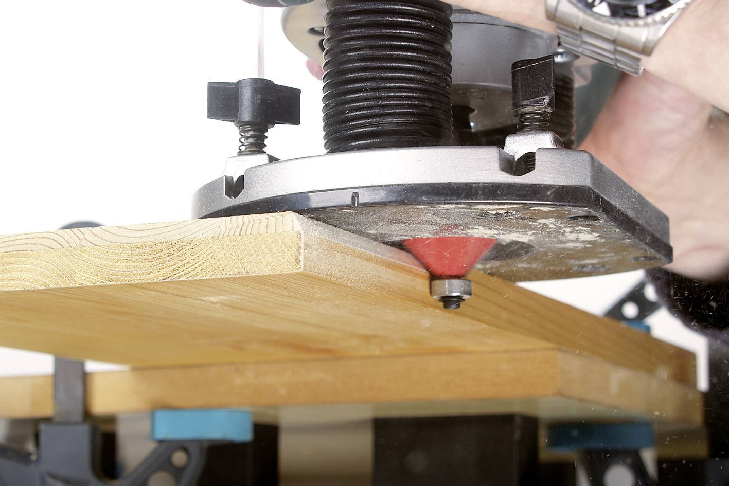 Quelqu'un utilise une défonceuse pour arrondir le bord d'une planche. La planche est fixée dans un établi.