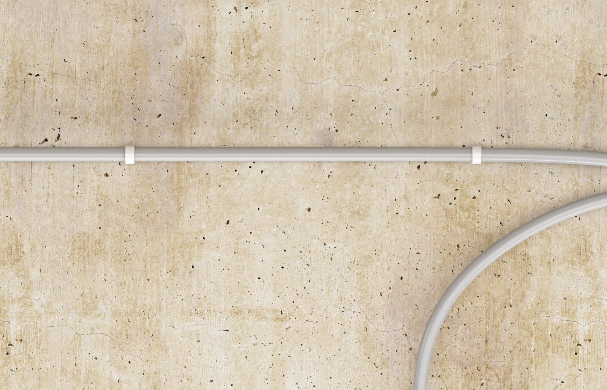 Câble blanc fixé avec des pinces s'étendant horizontalement sur un mur en béton beige, avec un segment de câble courbe entrant par le bas à droite.