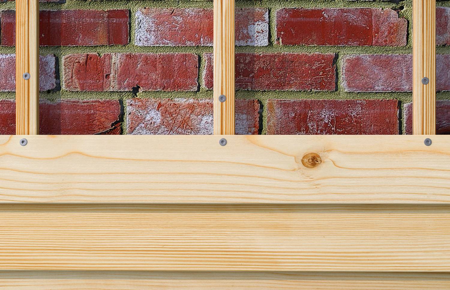 Gros plan d'une clôture en planches de bois clair avec des poteaux verticaux devant un mur de briques rouges.
