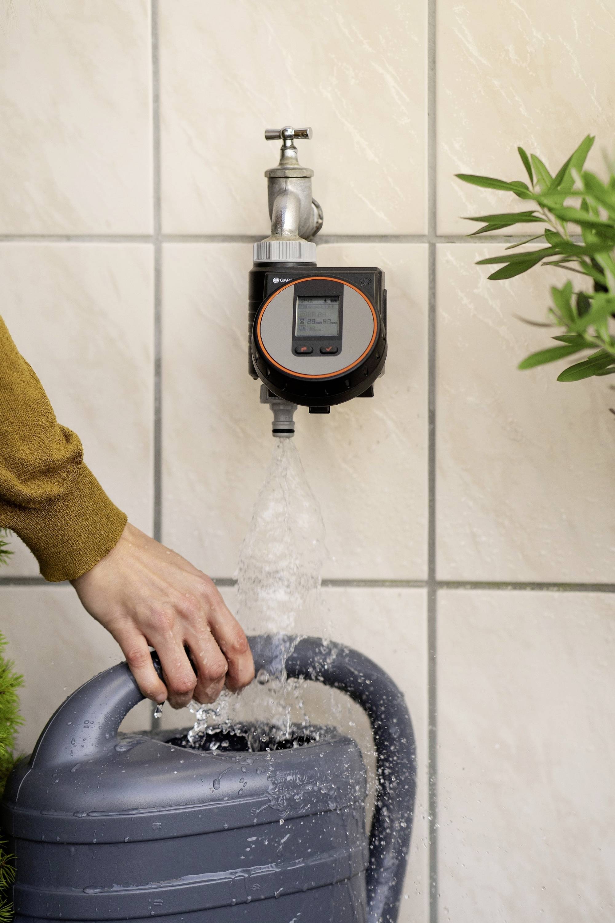 Une main remplit un arrosoir avec de l'eau provenant d'un robinet équipé d'un compteur d'eau.