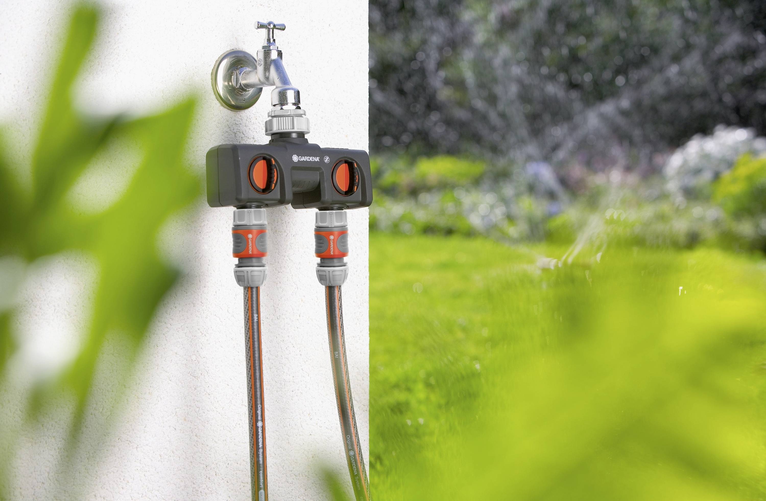 Deux tuyaux d'arrosage reliés à un programmateur d'irrigation arrosent la pelouse et les plantes à l'arrière-plan.