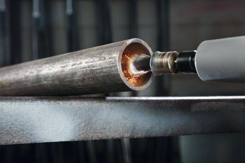 Gros plan d'un tube métallique en cours d'usinage avec un outil de forage. L'intérieur du tube brille d'une teinte cuivrée.