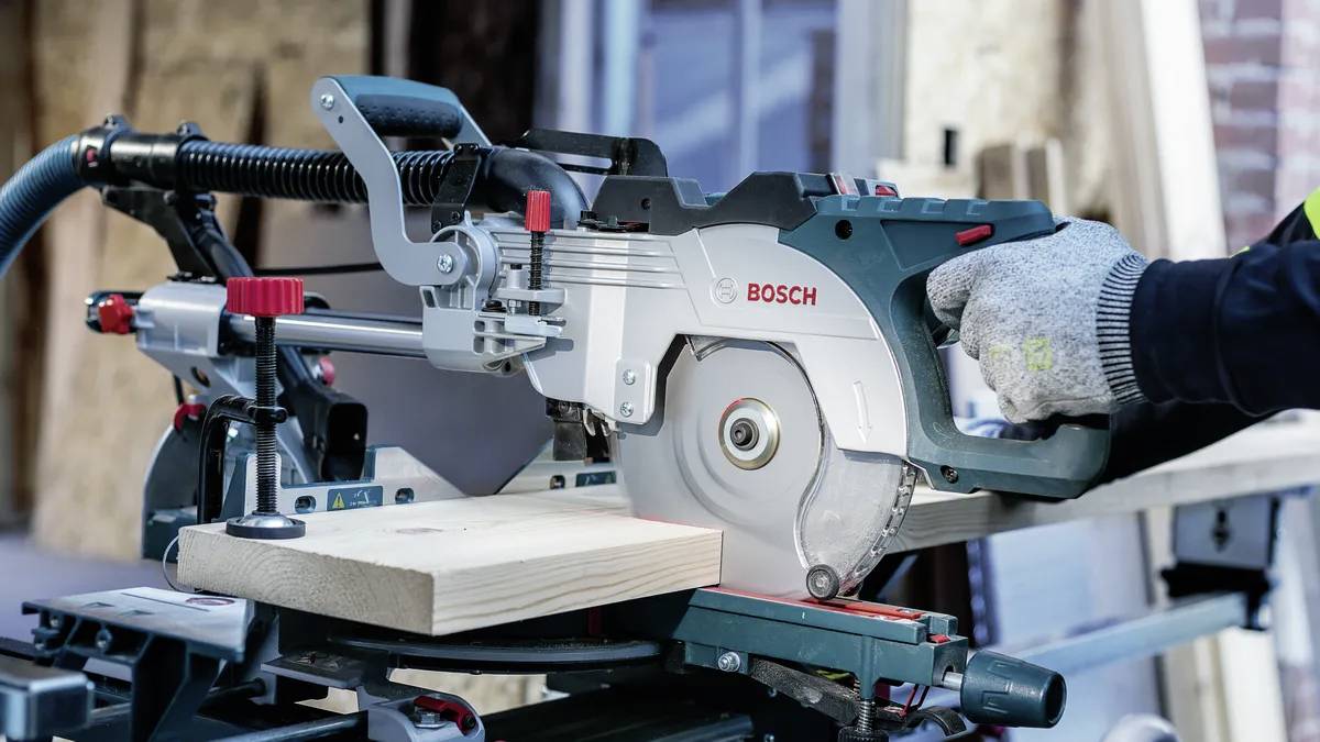 Une personne portant des gants utilise une scie circulaire Bosch pour couper une planche en bois, en soulignant la sécurité et la précision dans le travail du bois.