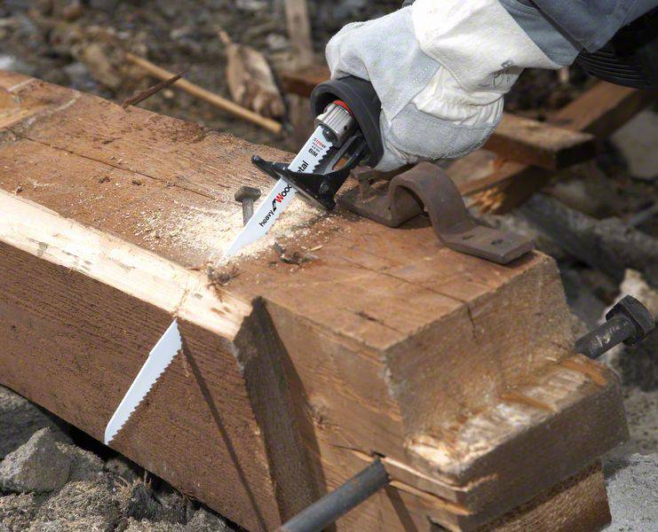 Une personne scie un grand morceau de bois avec une scie à main. Des copeaux de bois volent autour de la zone de coupe. Travaille à l'extérieur.