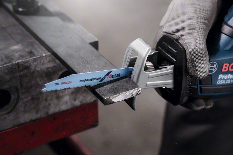 Une scie électrique coupe à travers un morceau de métal. Une personne tient fermement la scie tandis que le métal repose sur une table.