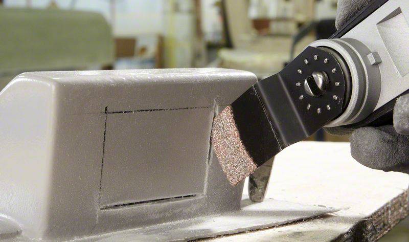 Un outil électrique muni d'une feuille abrasive lisse la surface d'une pièce métallique rectangulaire. L'arrière-plan montre un environnement d'atelier.