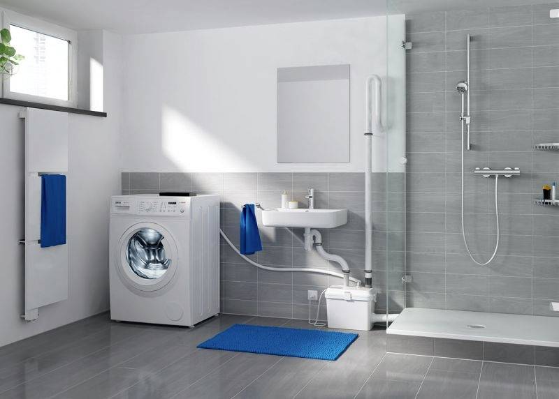 Salle de bain lumineuse avec des carreaux gris, un lave-linge à gauche, un petit lavabo au centre et une douche ouverte à droite.