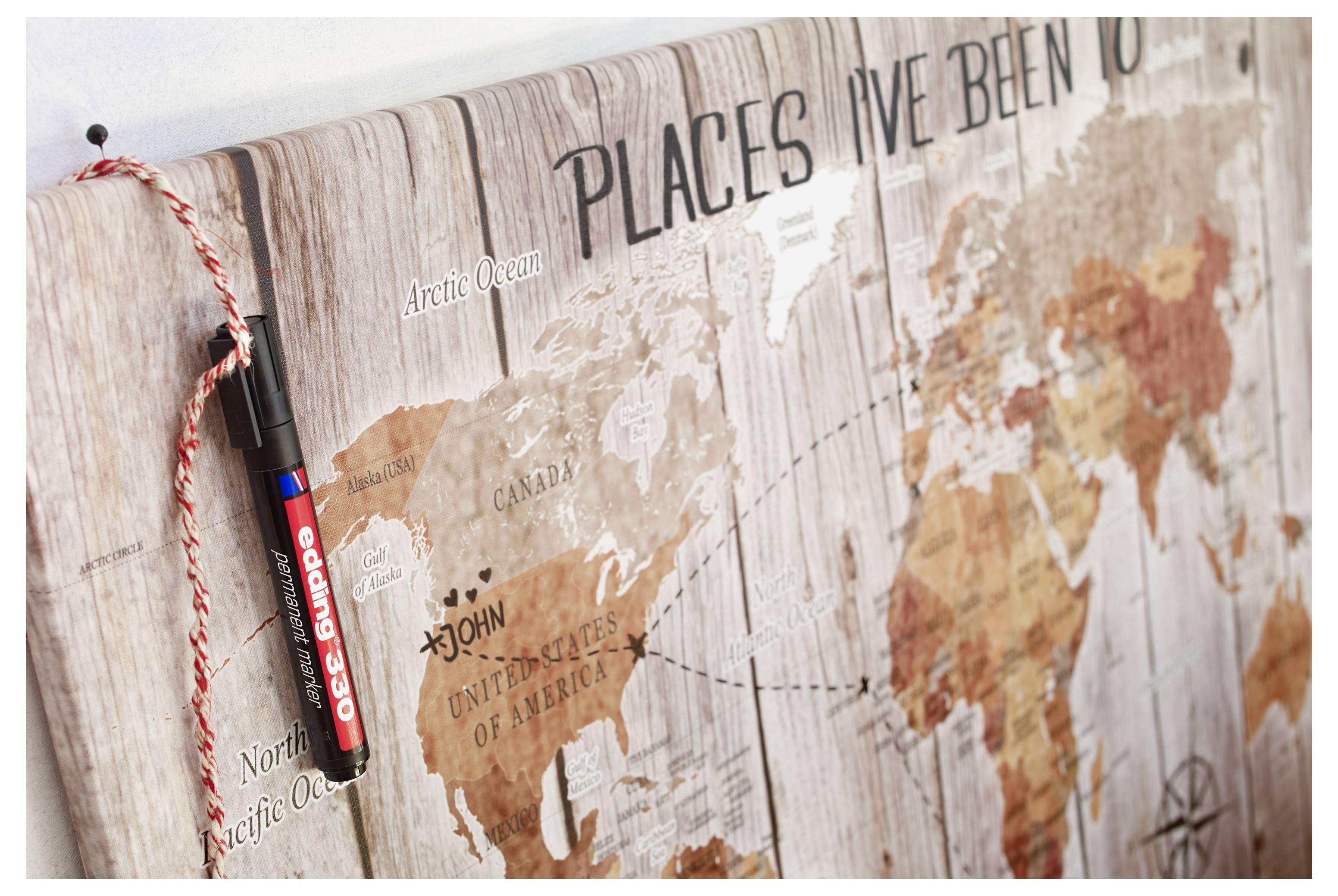 Gros plan d'une carte murale du monde en bois intitulée « Les endroits où j'ai été » avec un marqueur rouge et noir suspendu à côté pour marquer les lieux visités.