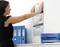 Une femme accroche un calendrier avec les mois de juillet à septembre au mur. À côté d'elle, des classeurs bleus sont posés sur une armoire.