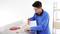 Un homme portant un pull bleu coupe du ruban isolant sur une table de travail. Des étagères et des cartons sont visibles en arrière-plan.