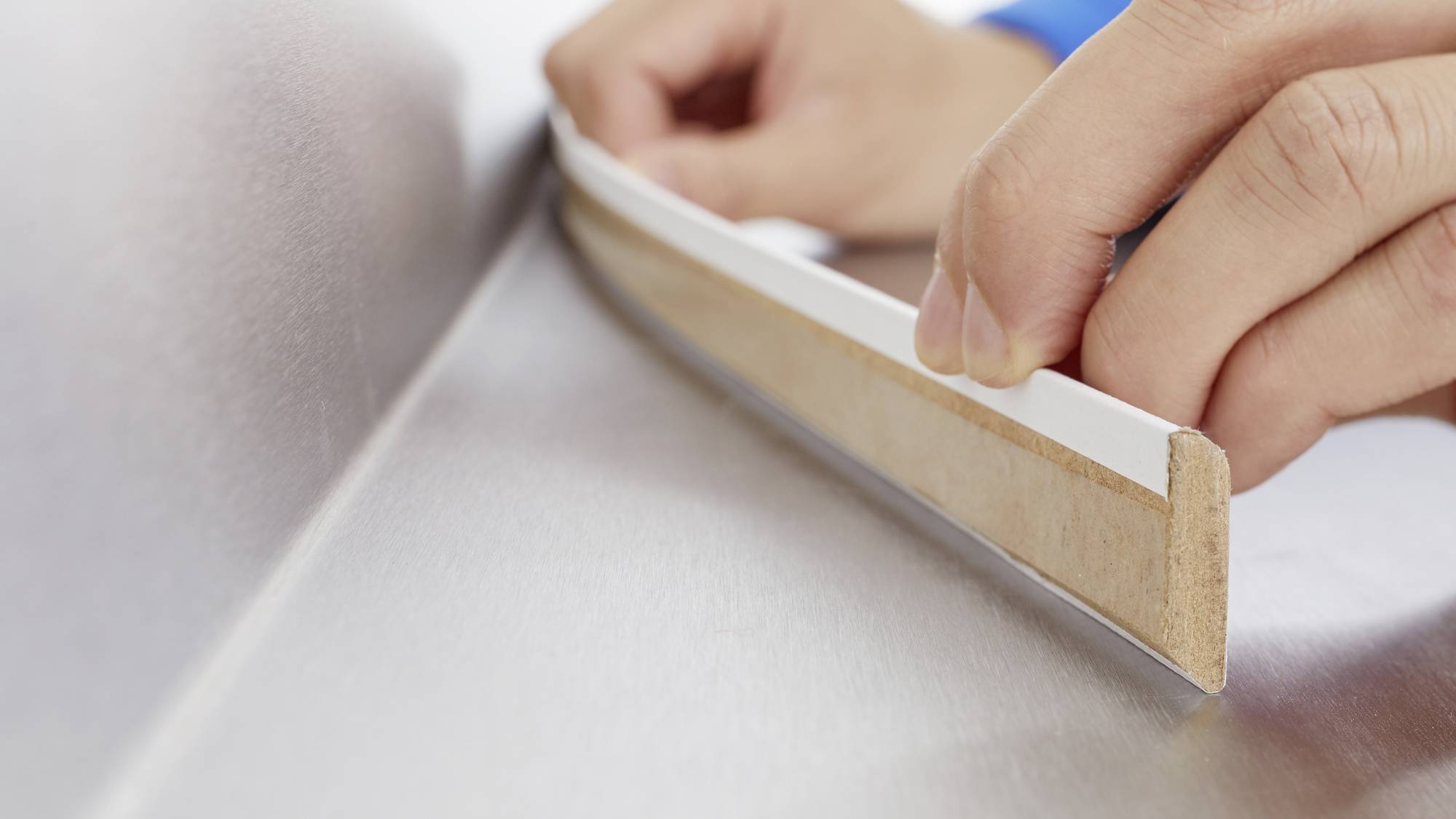 Une personne colle une bande d'étanchéité sur une surface lisse. La bande est soigneusement appliquée le long d'un bord.