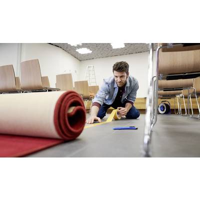 Un homme pose de la moquette dans une salle de conférence. Il est à genoux sur le sol et utilise du ruban adhésif. Des chaises sont visibles en arrière-plan.