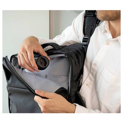 Un homme tenant un sac à dos noir ouvert et inspectant un appareil circulaire caché à l'intérieur, suggérant une recherche ou une vérification de sécurité.