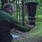 Une personne ajuste un piège à insectes noir dans un environnement forestier, avec des arbres et des broussailles en arrière-plan, indiquant une activité de recherche.