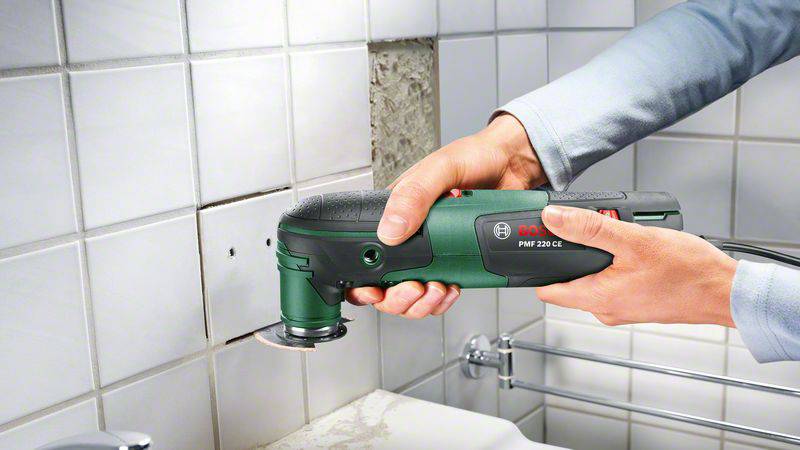 Une personne retire avec précision une tuile endommagée d'un mur de salle de bain à l'aide d'un outil multifonction oscillant, démontrant un travail soigné et technique.
