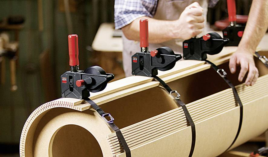 Une personne utilise trois pinces rouges pour fixer des pièces de bois rondes et volumineuses. Les pinces sont placées le long de la courbure.