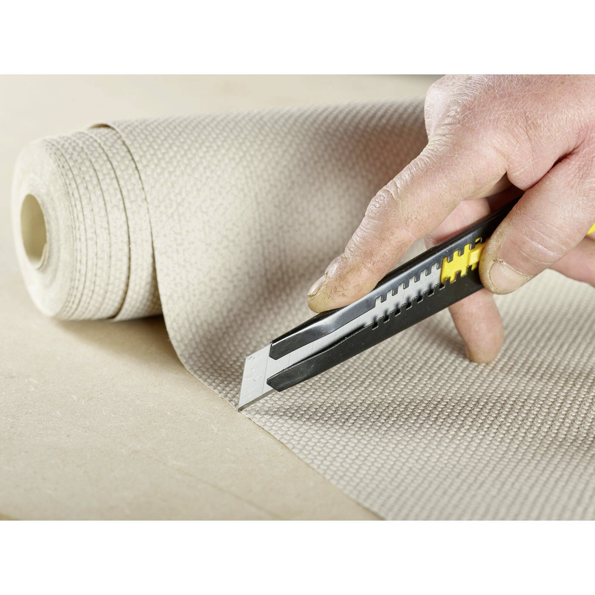 Une main coupe un tapis avec un cutter sur une surface plane.