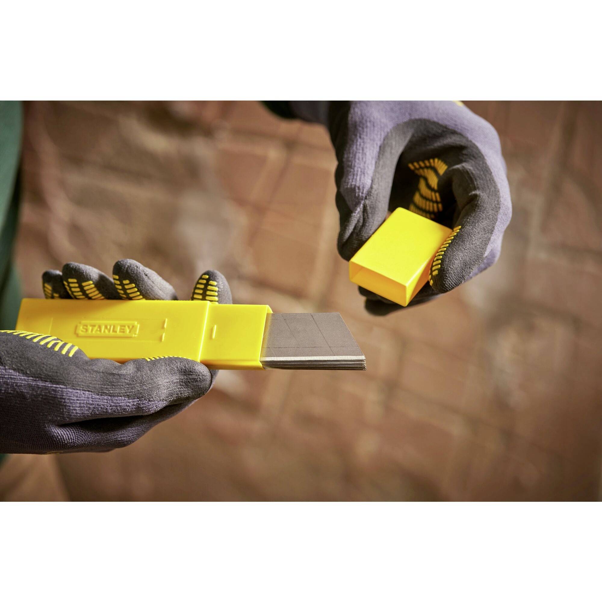 Deux mains gantées tiennent un ciseau jaune. Une main retire le capuchon de protection des lames noires.