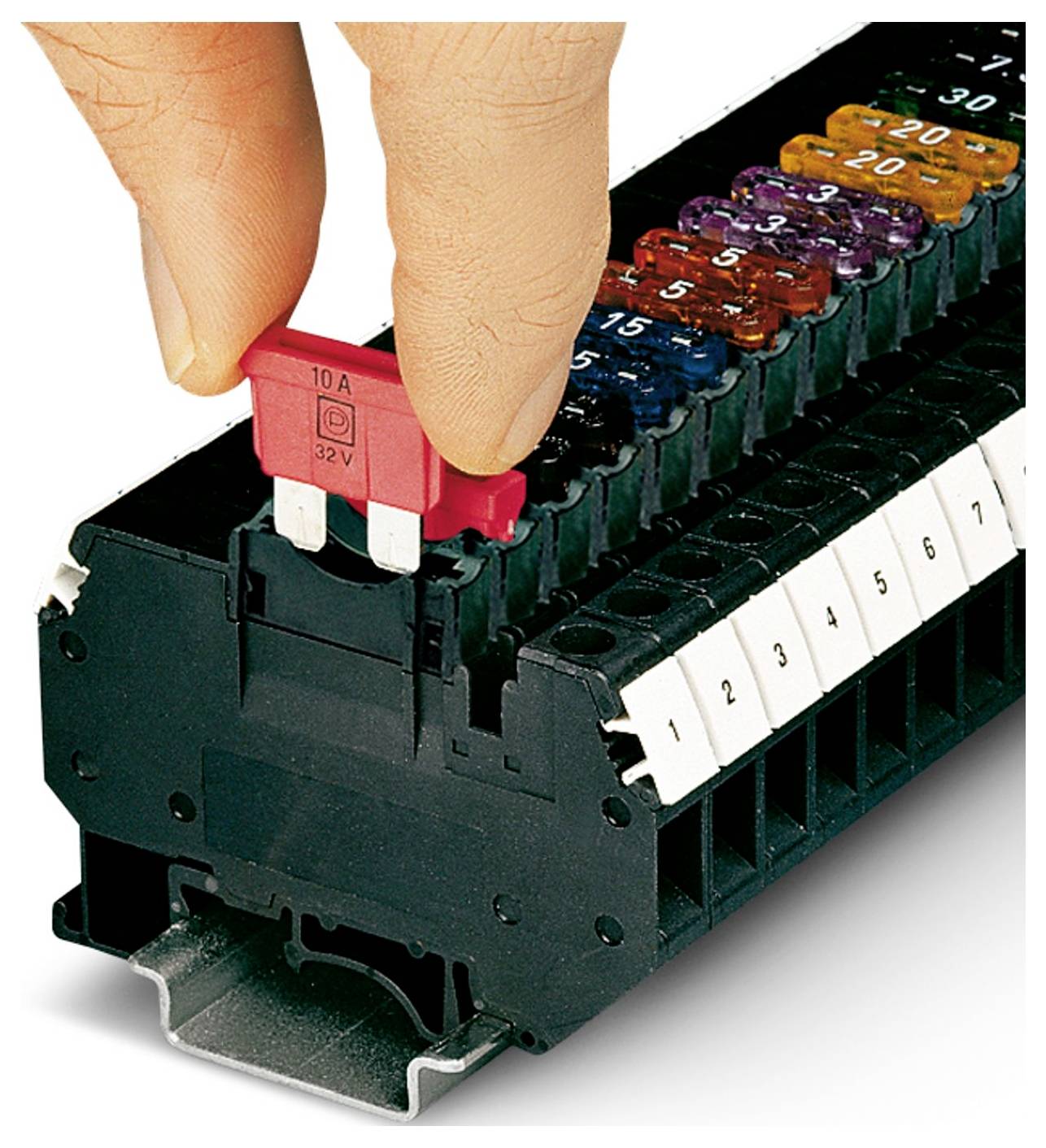 Une main insère un fusible rouge 10A 32V dans un bloc de fusibles contenant plusieurs fusibles de couleurs différentes. Le bloc est étiqueté numériquement de 1 à 10.