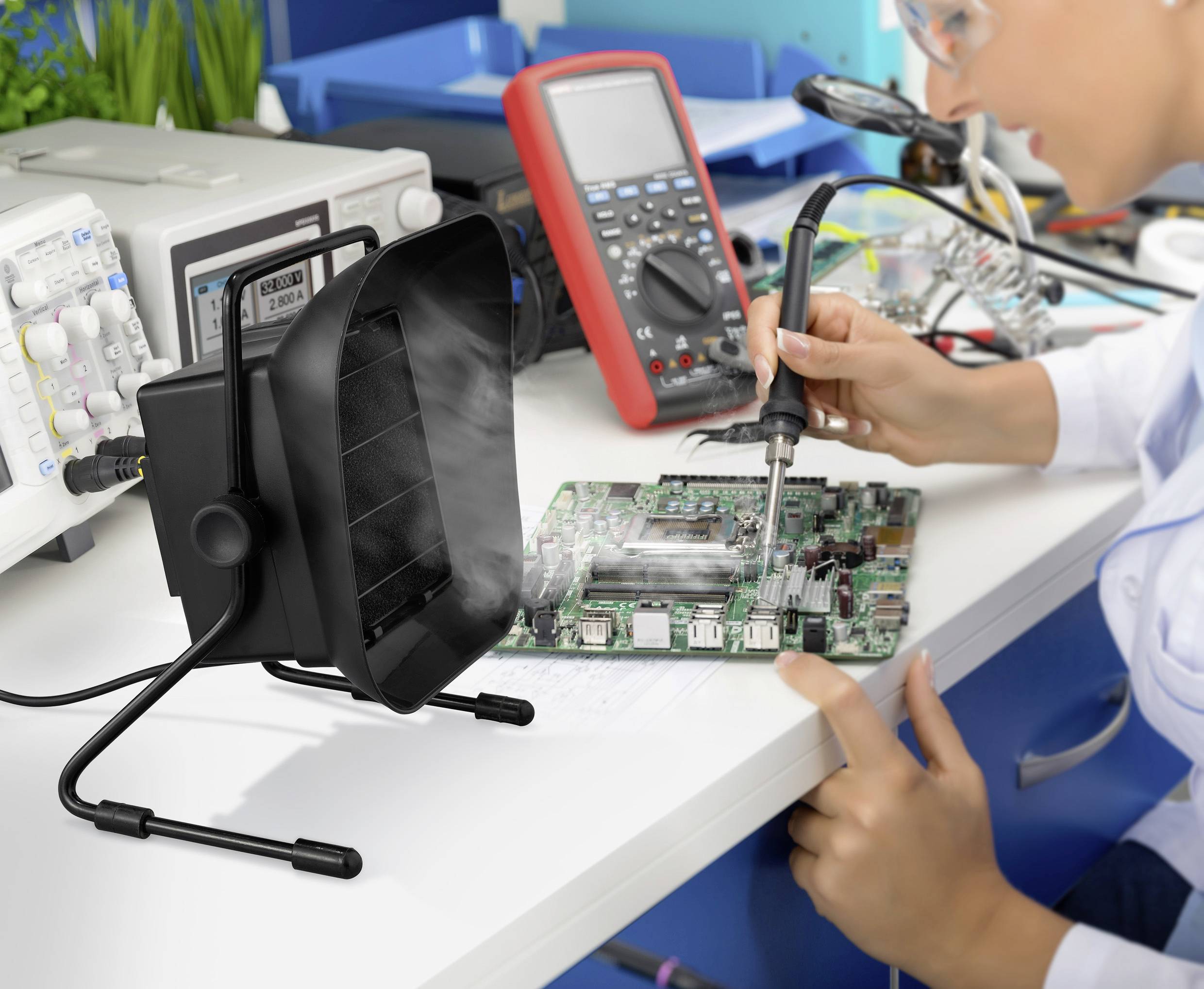 Une personne soude sur une carte de circuit imprimé dans un environnement de laboratoire, avec un dispositif d'extraction de fumée et des instruments de mesure en arrière-plan.
