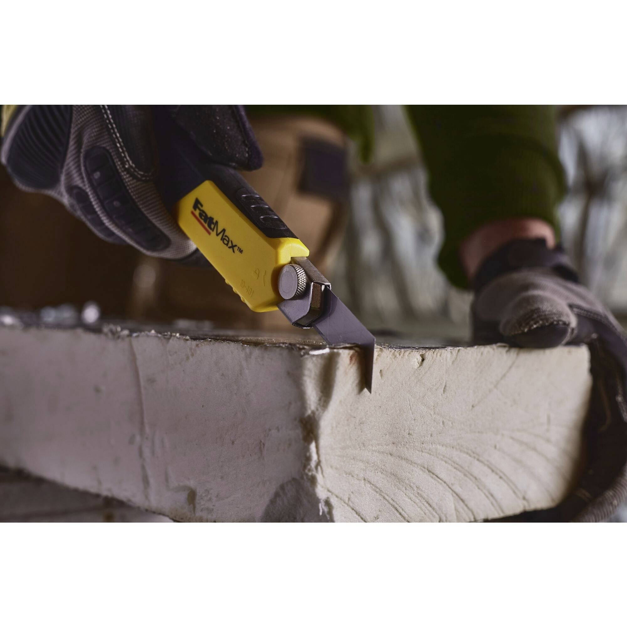 Une personne coupe dans un bloc de béton gris à l'aide d'un cutter jaune. La personne porte des gants de protection.