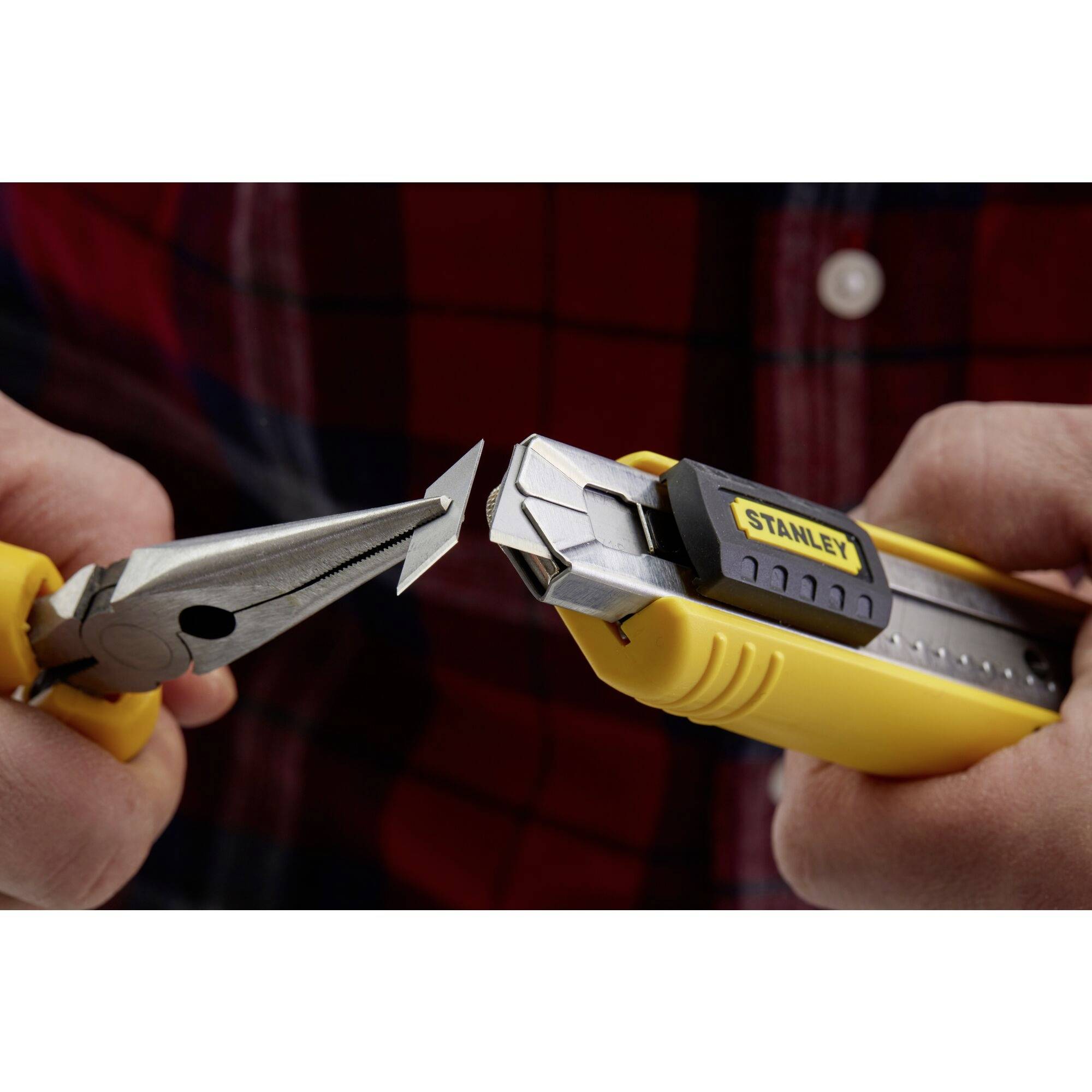 Une personne coupe un morceau de métal gris avec un cutter jaune Stanley, maintenu par une pince.