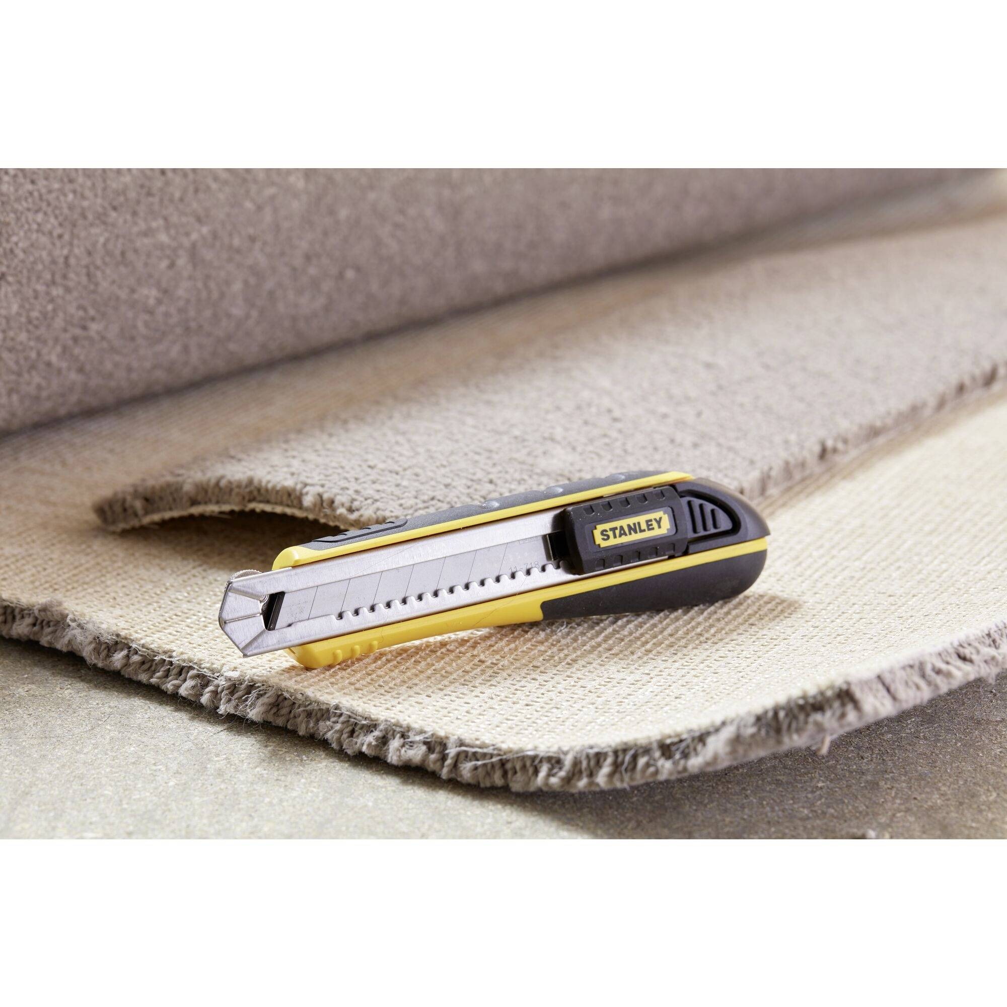 Un couteau à tapis repose sur un rouleau de moquette partiellement découpé, prêt à être coupé. L'arrière-plan est constitué de moquette.