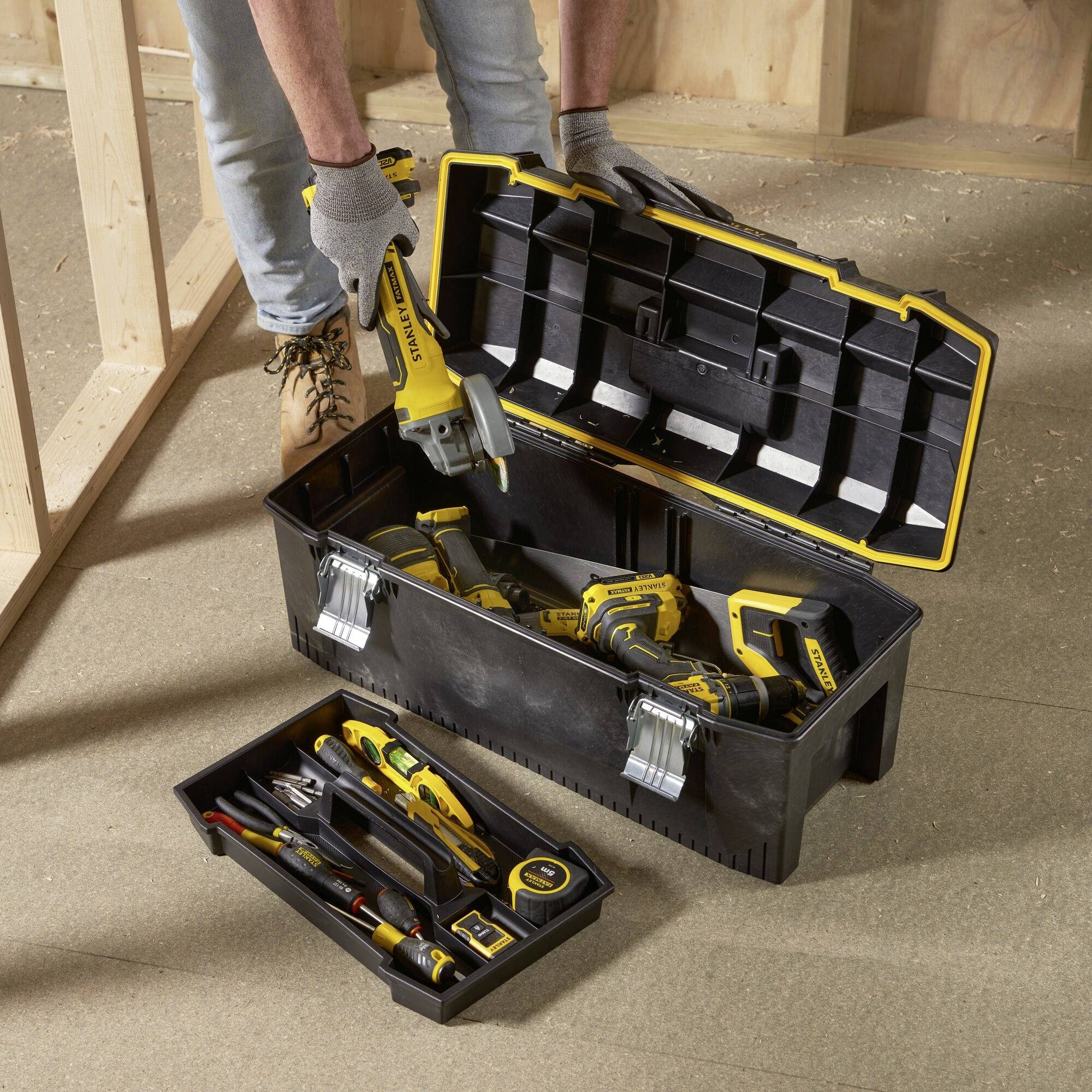 Une boîte à outils ouverte contenant divers outils électriques et manuels. Une personne en sort un outil électrique.