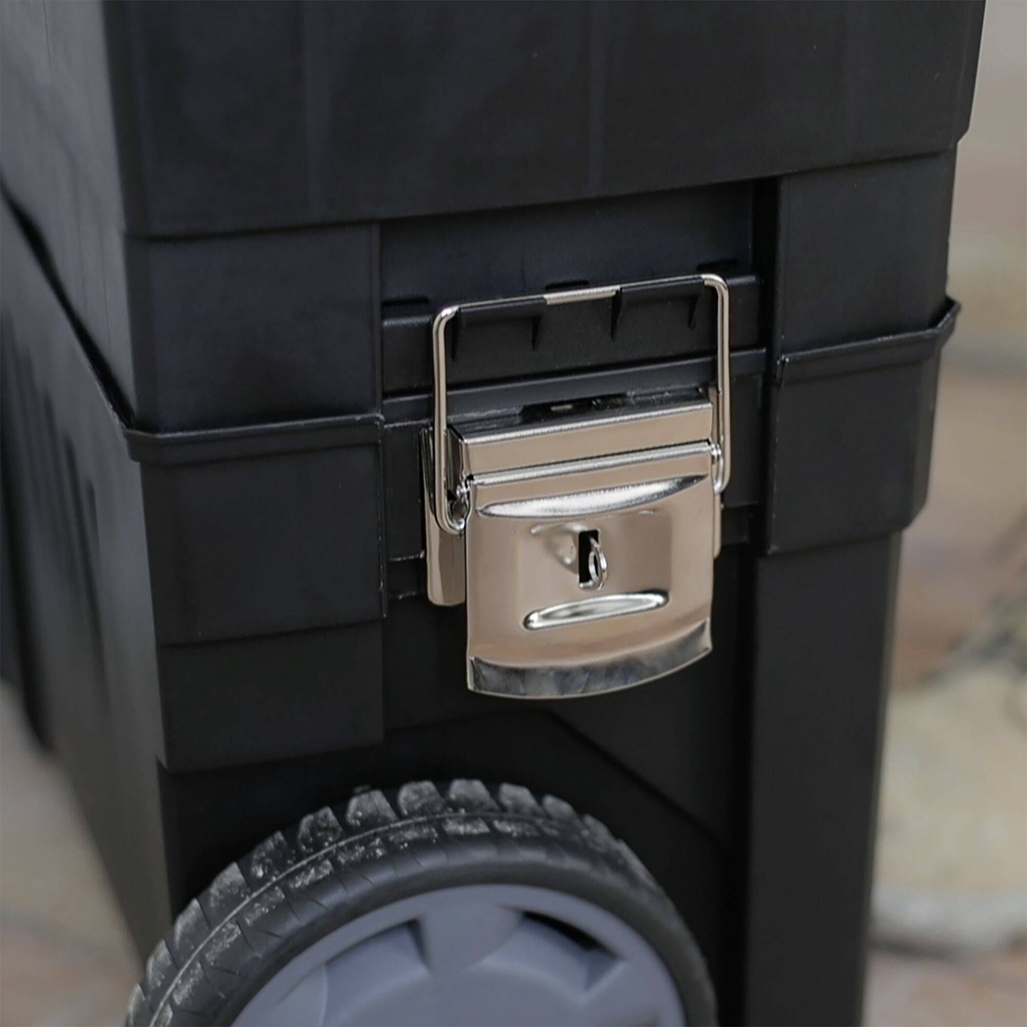 Boîte à outils noire avec fermeture argentée et grandes roues sur surface claire.